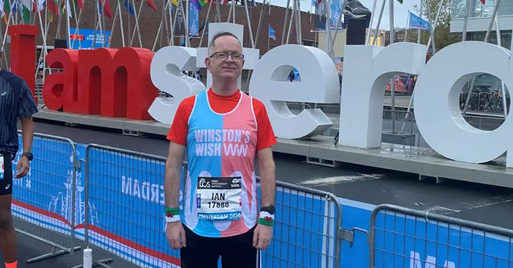 Ian wearing a Winston's Wish running vest in front of the I am Amsterdam sign