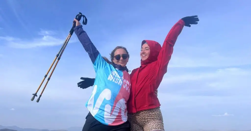 Matilda with her mum Melody with their arms raised at the top of the peaks, celebrating their success