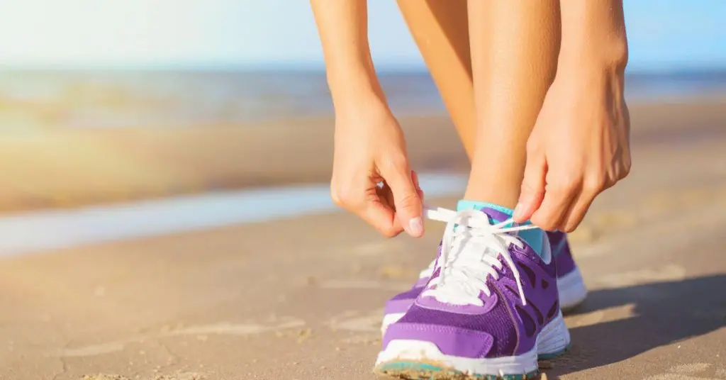 A person tying their running shoe at the beach