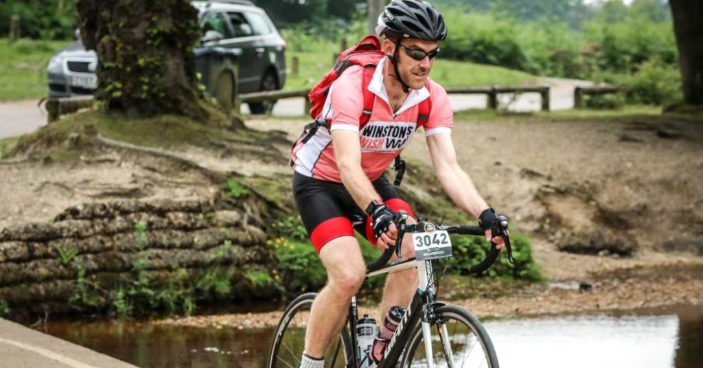 Russ cycling over a small bridge while wearing a Winston's Wish branded t-shirt
