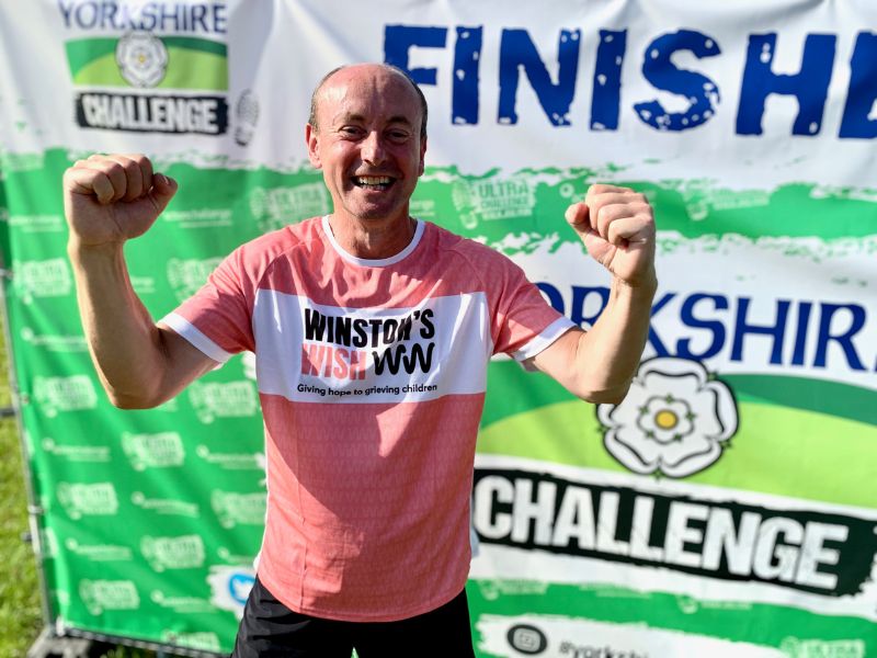 man cheering at finish line of yorkshire ultra challenge in winston's wish jersey