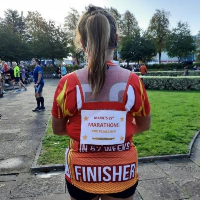 Marie with a sign on her back that celebrates her 99th marathon