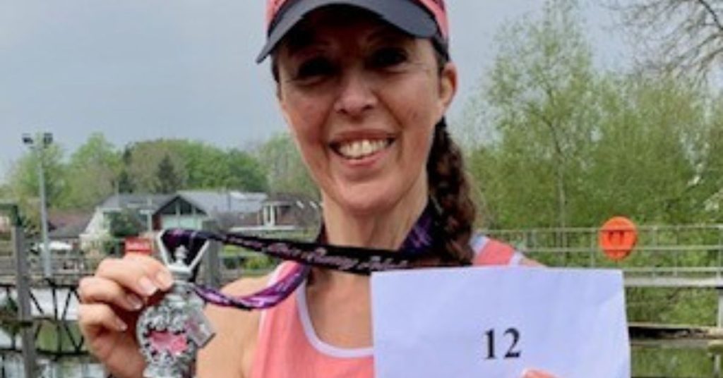 Liz at the finish line holding her medal and a sign that reads '12' marking her last half marathon challenge